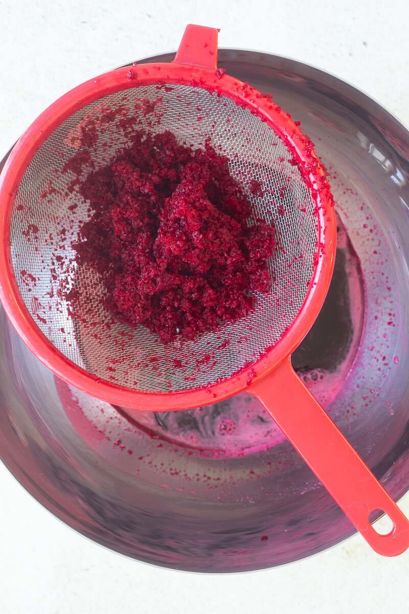 Blended beetroots being strained into a large silver bowl.