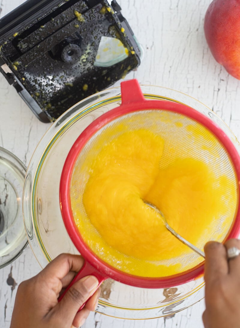 An image of me holding a strainer to get get the juice from the blended mango.