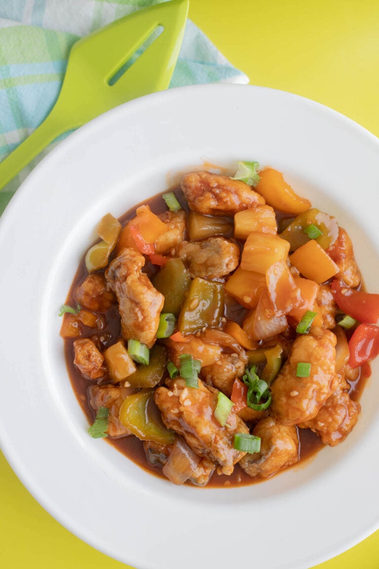 Sweet and sour fish in a white bowl with a checkered napkin on a green backdrop.