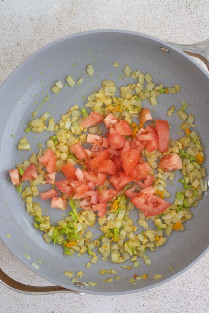 Tomatoes on top of fried aromatics in a frying pan.