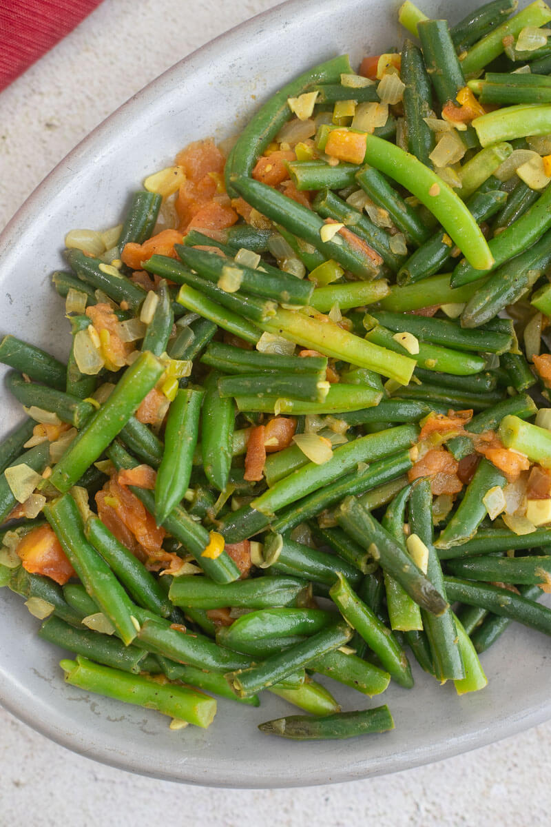 Close up of Trini fry bodi with aromatics and tomatoes on a silver plate.