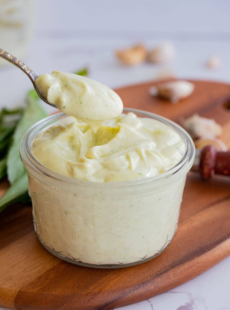 A bowl of mixed trini garlic sauce, with a lifted spoon of sauce to show details.
