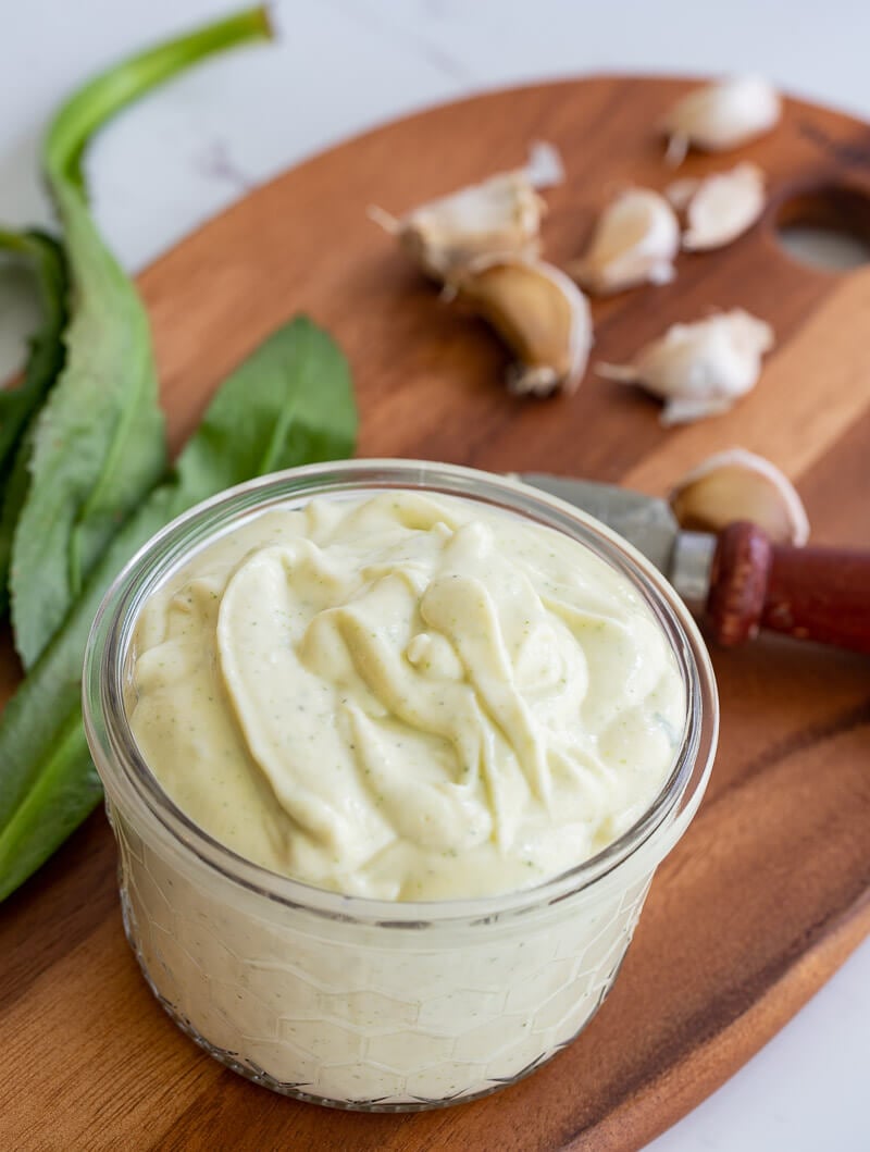 Close up of Trinidad garlic sauce in a clear bowl with chadon beni in the background.