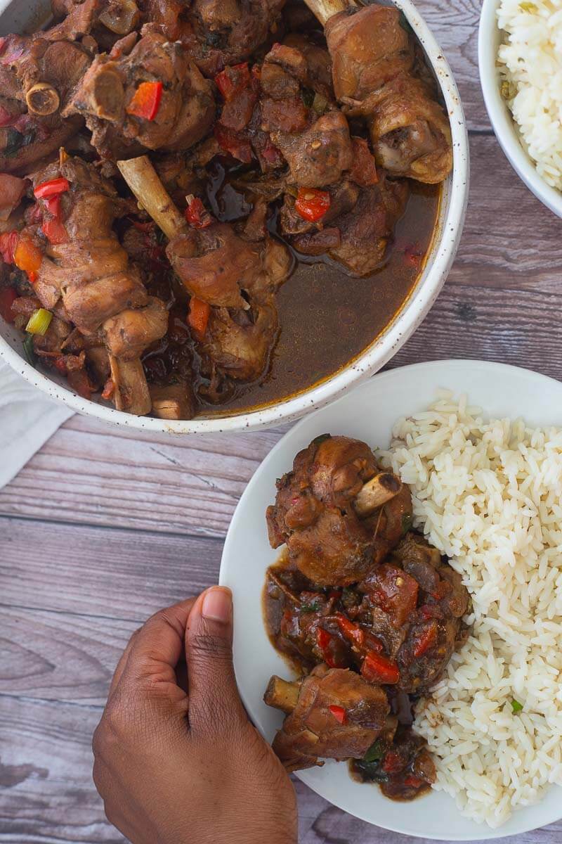 Stewed chicken trini style, in a large bowl being served with a side of white rice.