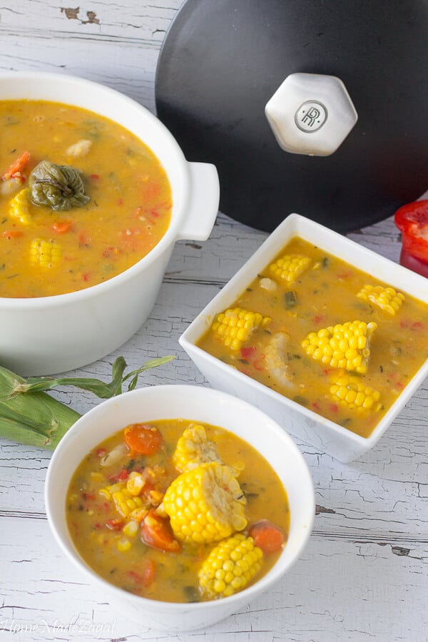 A large pot of corn soup with a bowl fulll of soup on a white background.