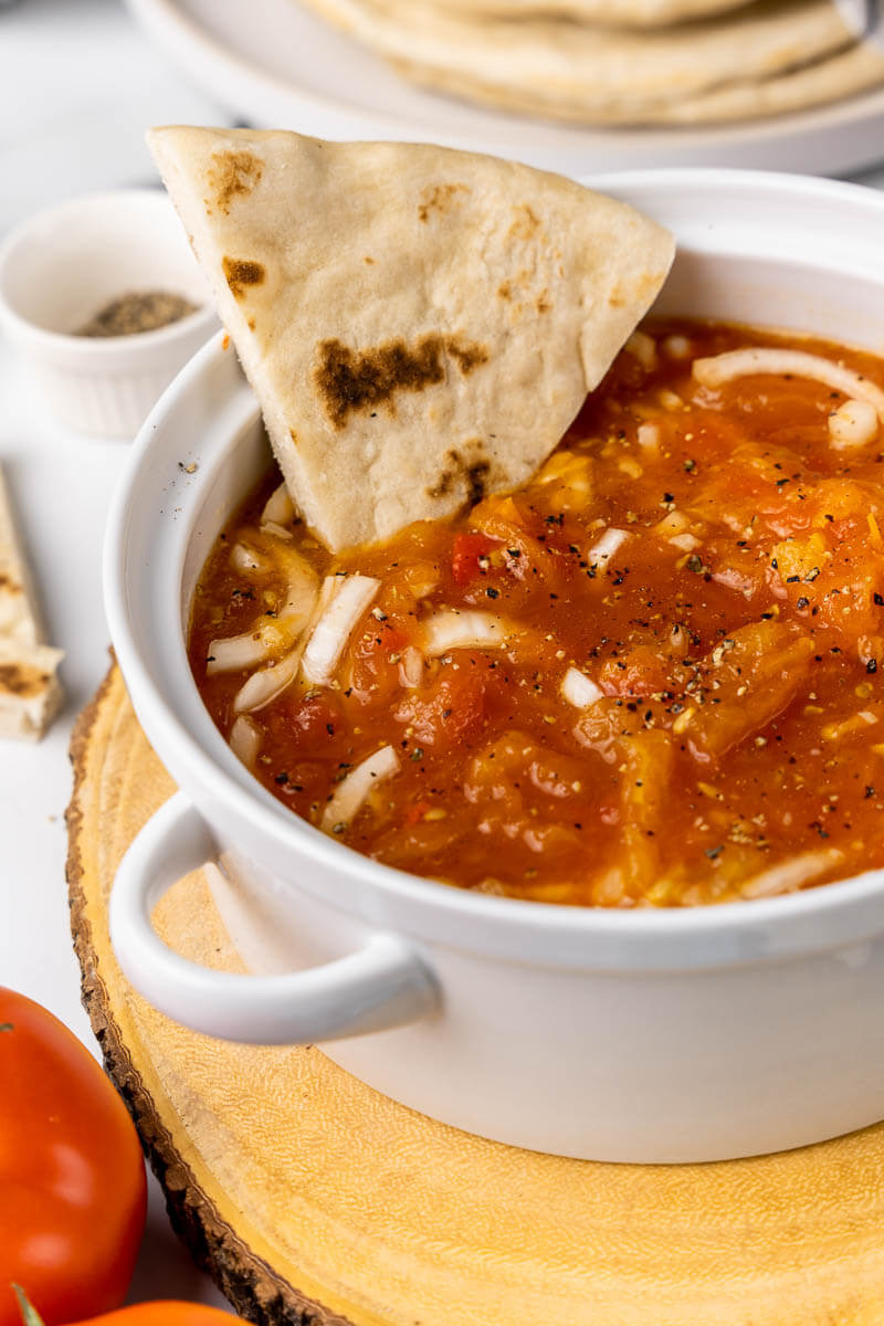 Close up of a full bowl of tomato choka with a slice of sada roti.