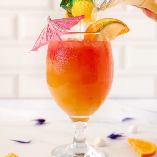 Pouring some rum into a glass adorned with garnishes.