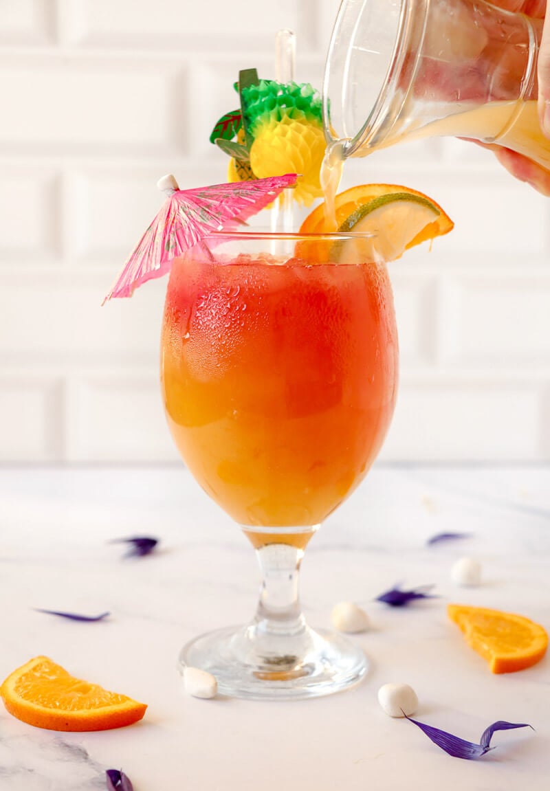 Pouring some rum into a glass adorned with garnishes.