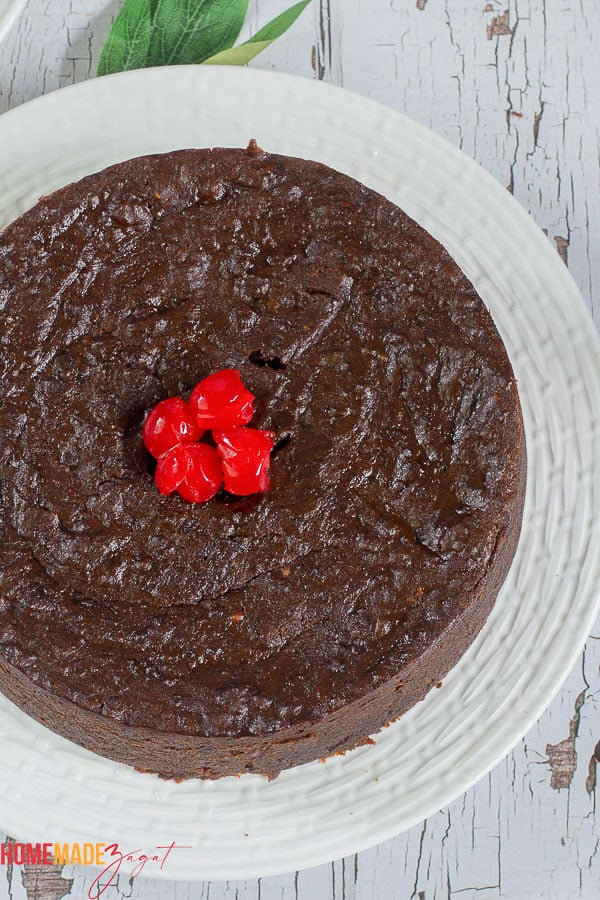 A whole black cake with red cherries on top resting on a white plate