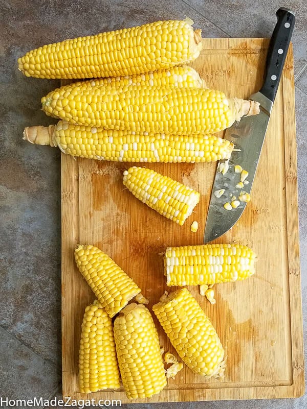 Corn cobs on a brown cutting board with a knife.