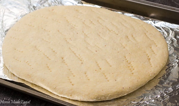 Flattened out coconut bake on a baking sheet with fork marks.