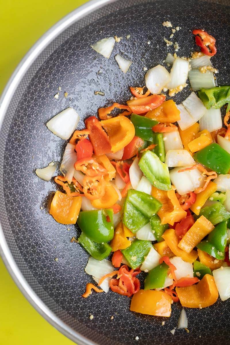 Peppers and other aromatics sautéing in butter in a black wok.