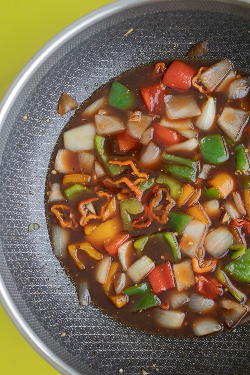 Vegetables in pineapple juice simmering in a black wok.