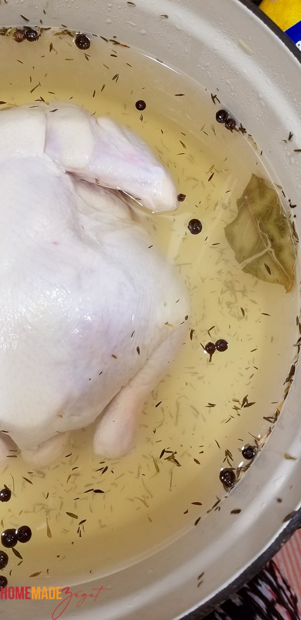 A whole chicken sitting in brine with bayleaves, pimento balls and dried thyme.