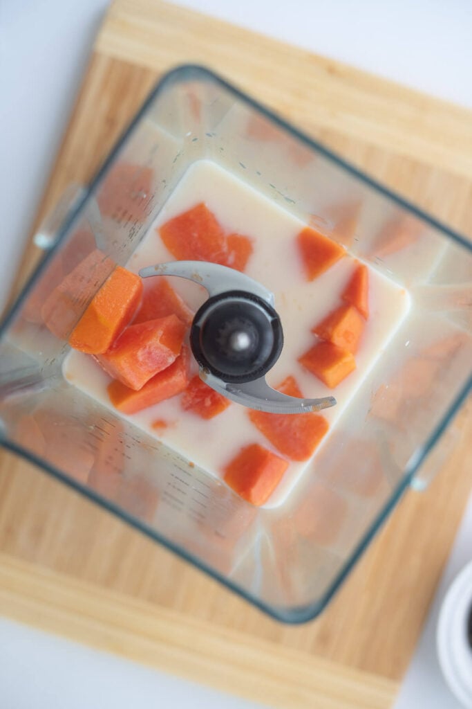 Blender with cubed pawpaw and milk ready to blend to prepare a creamy Caribbean drink.