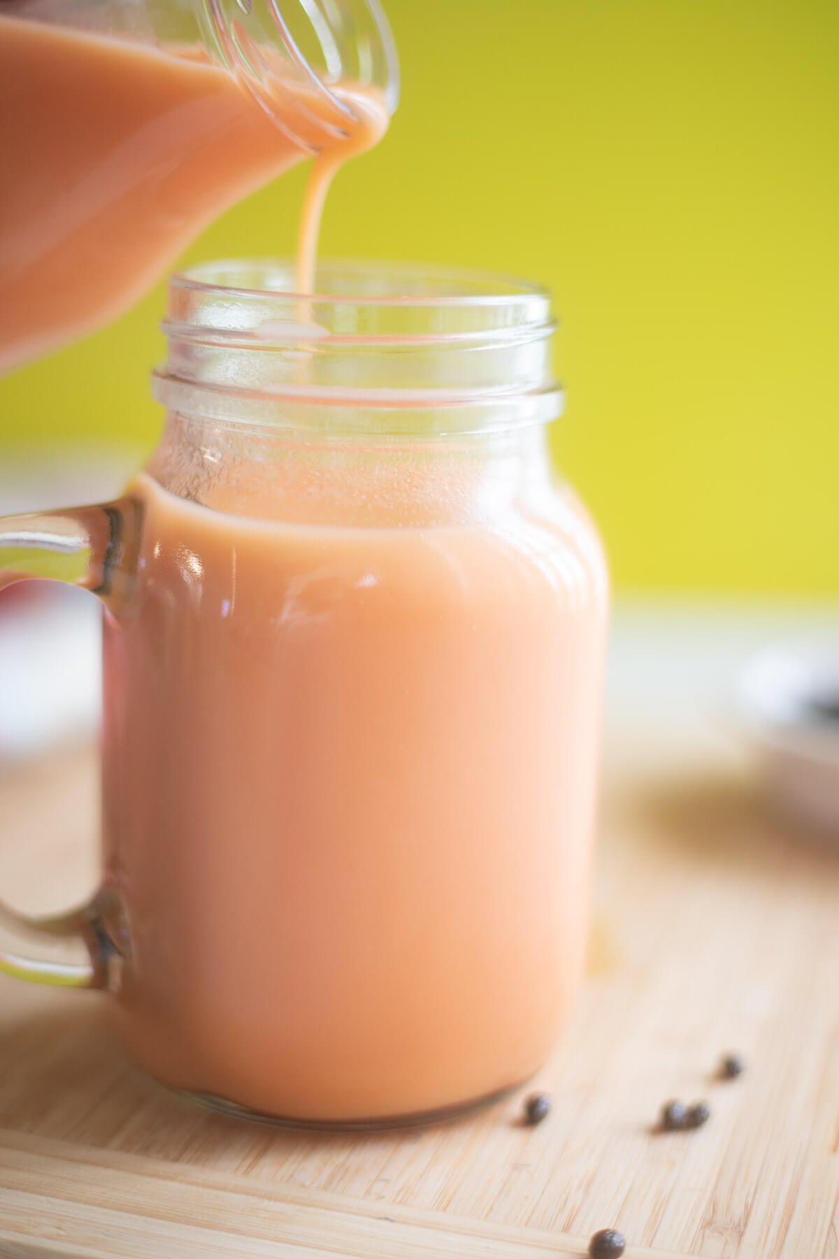 Pouring a creamy pawpaw drink from a glass bottle into a mason jar, perfect for a refreshing Caribbean treat.