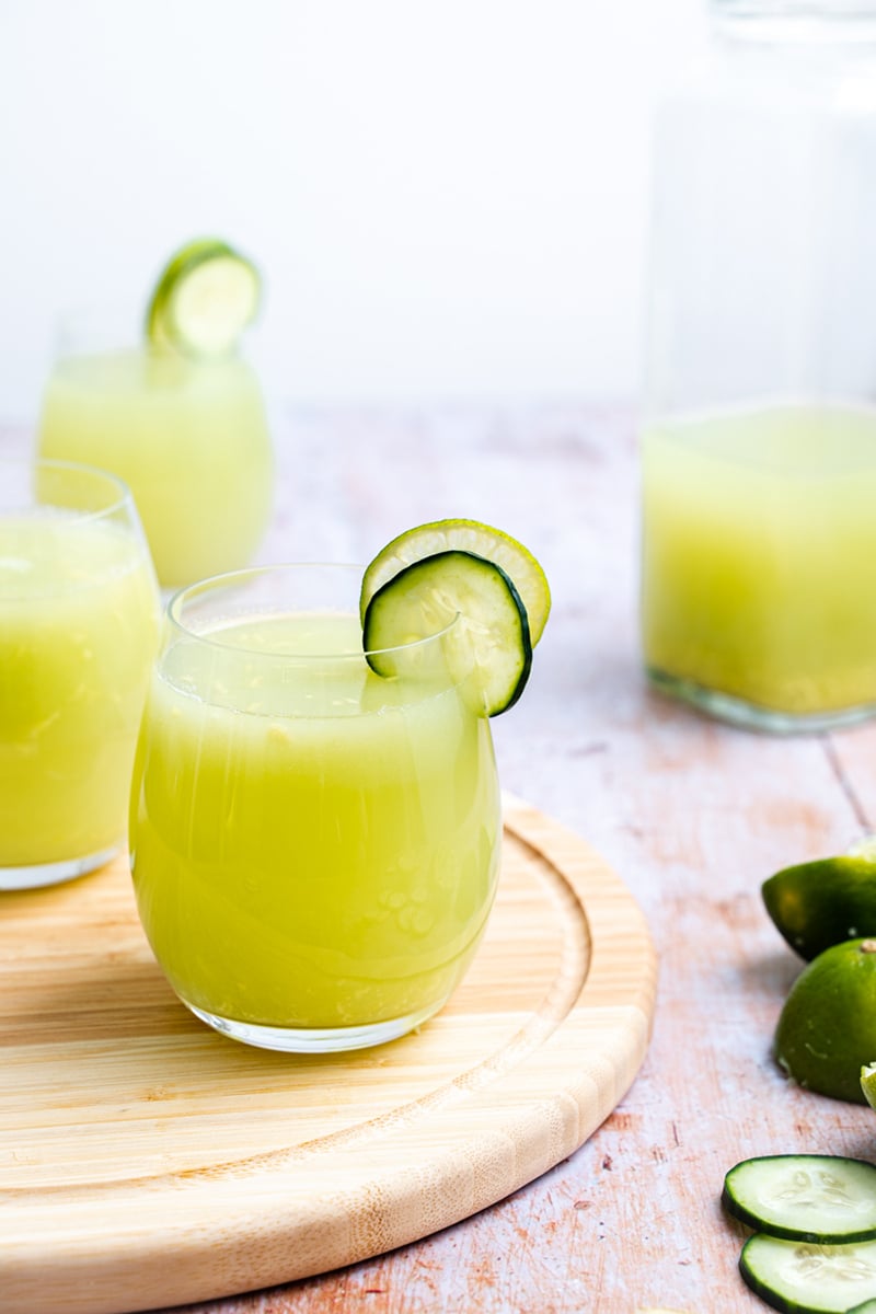 A chilled glass of cucumber and lime juice served with ice cubes, a lime wedge, and a cucumber slice for a cooling presentation.