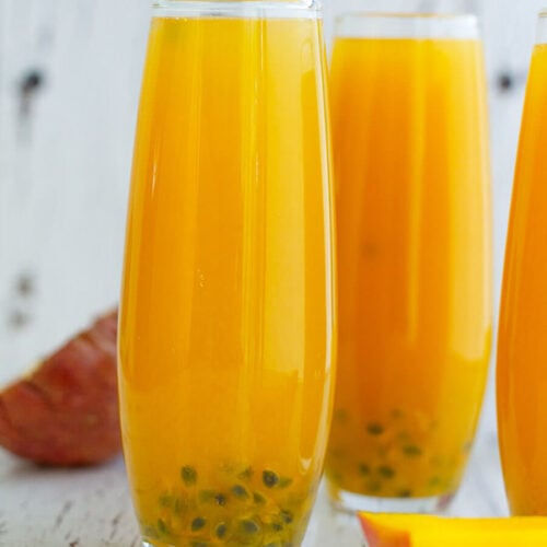 Three completed glasses of mango passion fruit juice with passion fruit seeds as a garnish.