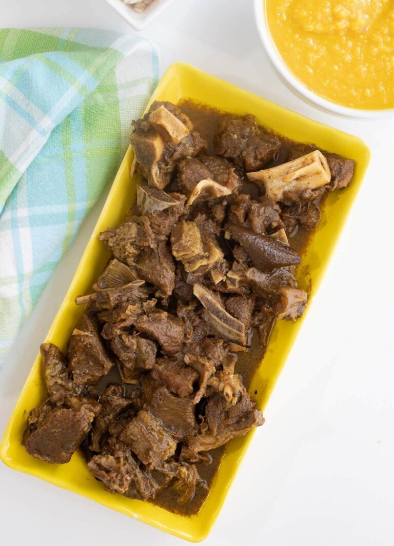 Cooked curry goat meat on a yellow plate on a white countertop.