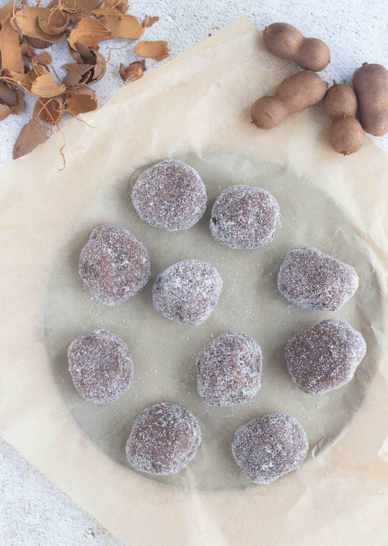 Tamarind balls on wax paper with tamarind shells on a textured background.