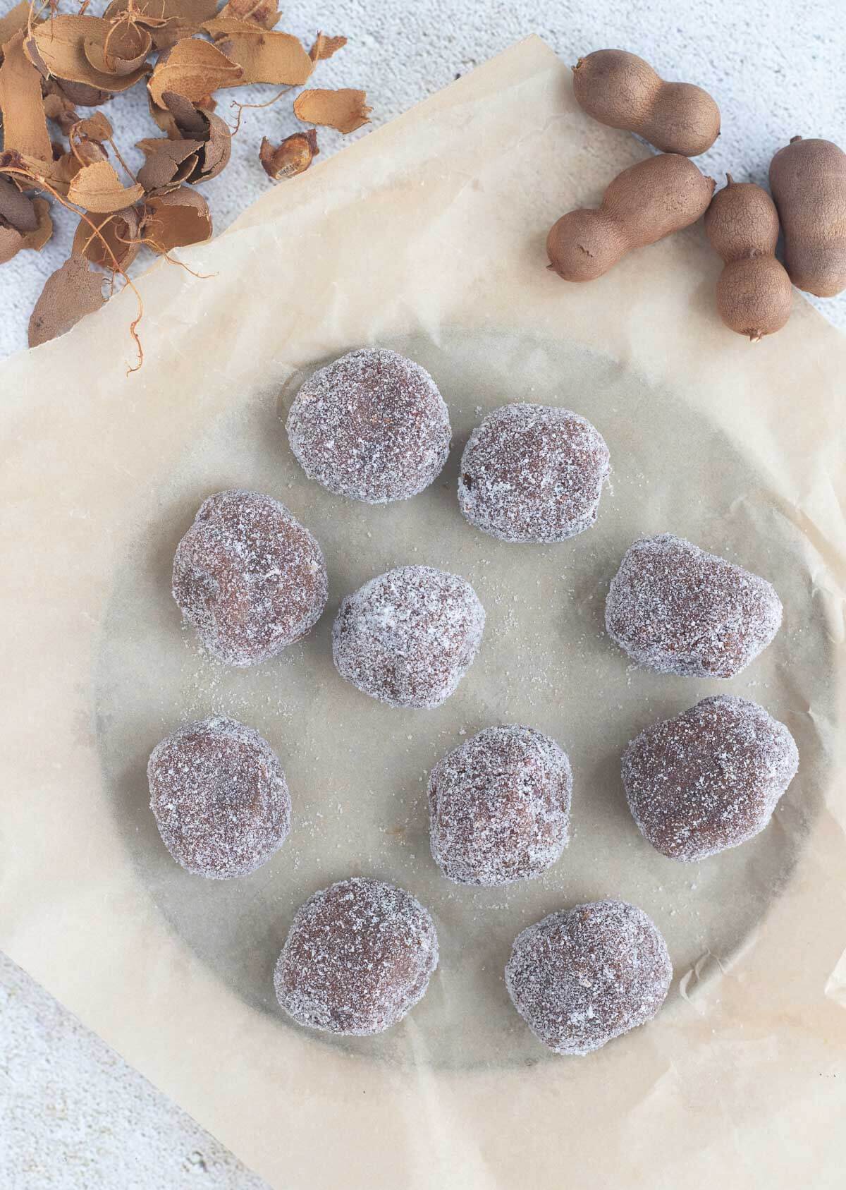Tamarind balls on wax paper with tamarind shells on a textured background.