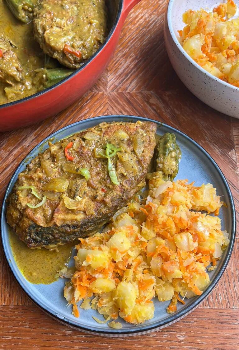 A pot of curry fish with a slice of fish and butter cassava on a plate.