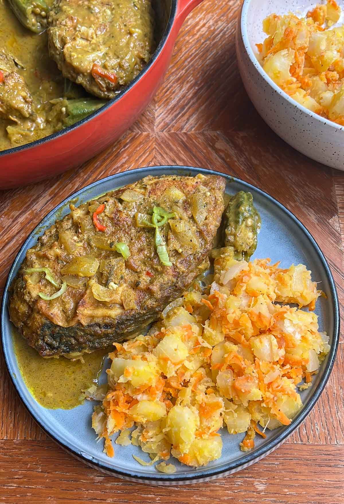 A pot of curry fish with a slice of fish and butter cassava on a plate.