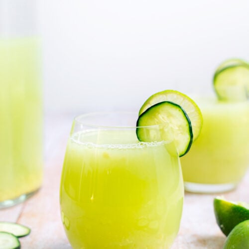 A refreshing glass of cucumber and lime juice with a garnish of lime and cucumber, perfect for hydrating on a hot summer day.