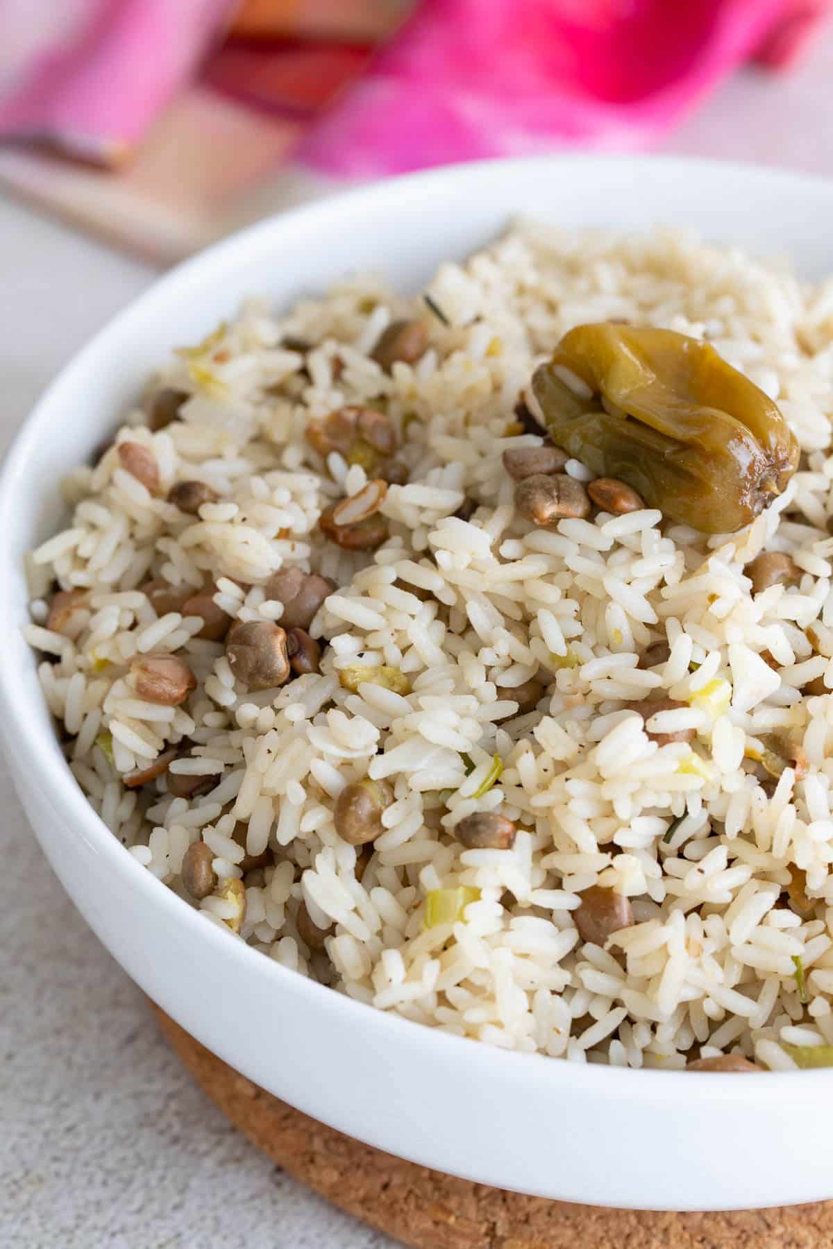 A white bowl on a brown board with pigeon peas and rice with a whole pepper sitting on the top.