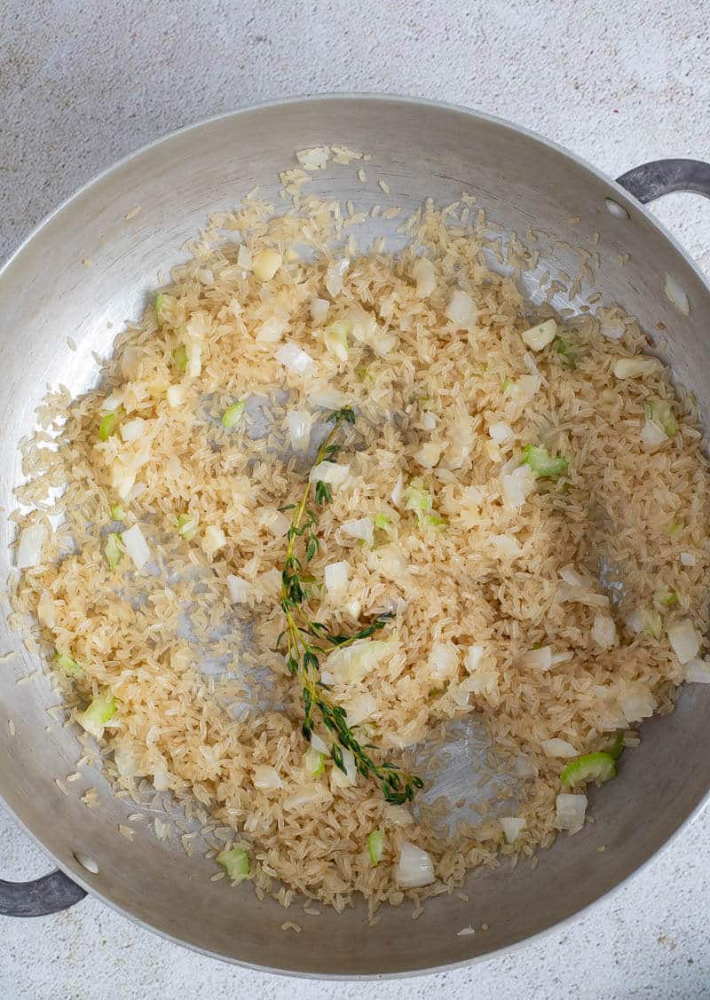 Parboiled rice added to aromatics along with fresh herbs.