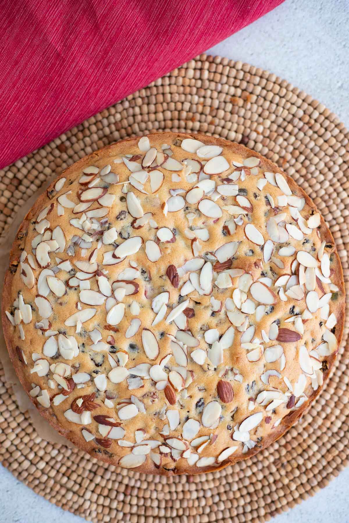 A whole Dundee cake on a brown mat with a red throw cloth.