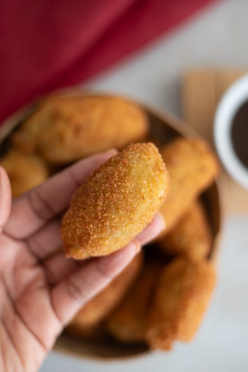 Hand holding a freshly fried saltfish ball with crispy crust.