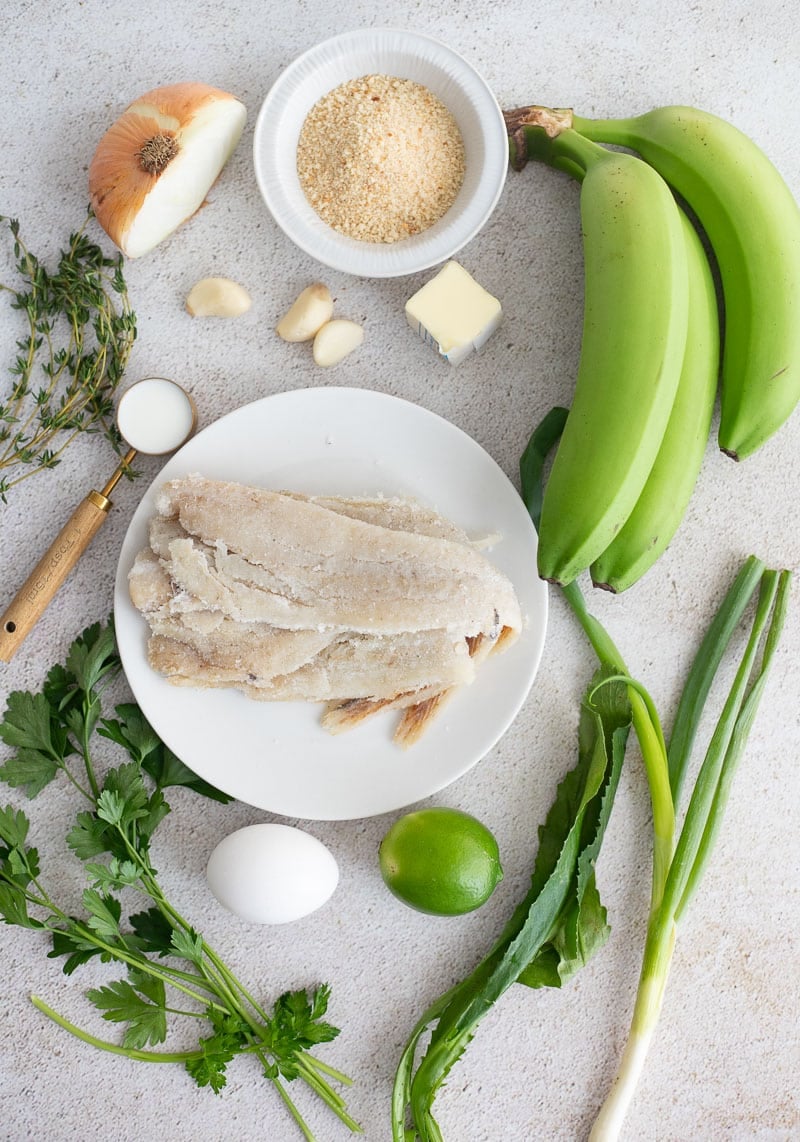 Ingredients for saltfish balls including saltfish, green bananas, herbs, breadcrumbs, and seasonings.
