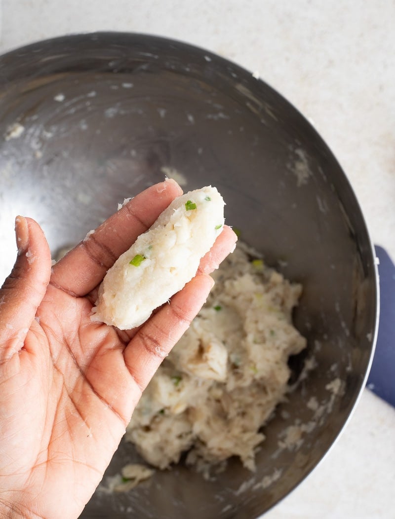 Hand shaping seasoned saltfish mixture into an oval ball.