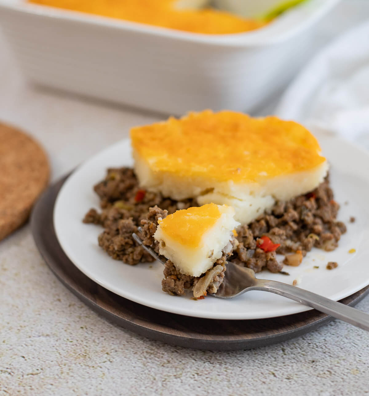 Close-up of a slice of Caribbean shepherd's pie made with mashed cassava and seasoned beef, served on a white plate with a fork.