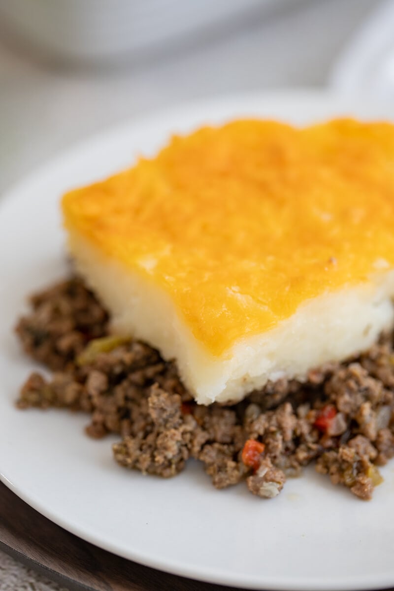Close-up view of a slice of Caribbean shepherd’s pie made with mashed cassava and a golden cheesy topping over seasoned beef filling