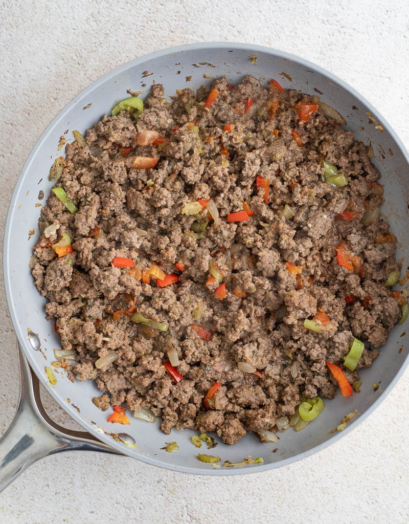 Ground beef filling cooked with sweet peppers, tomato, and celery in a skillet.