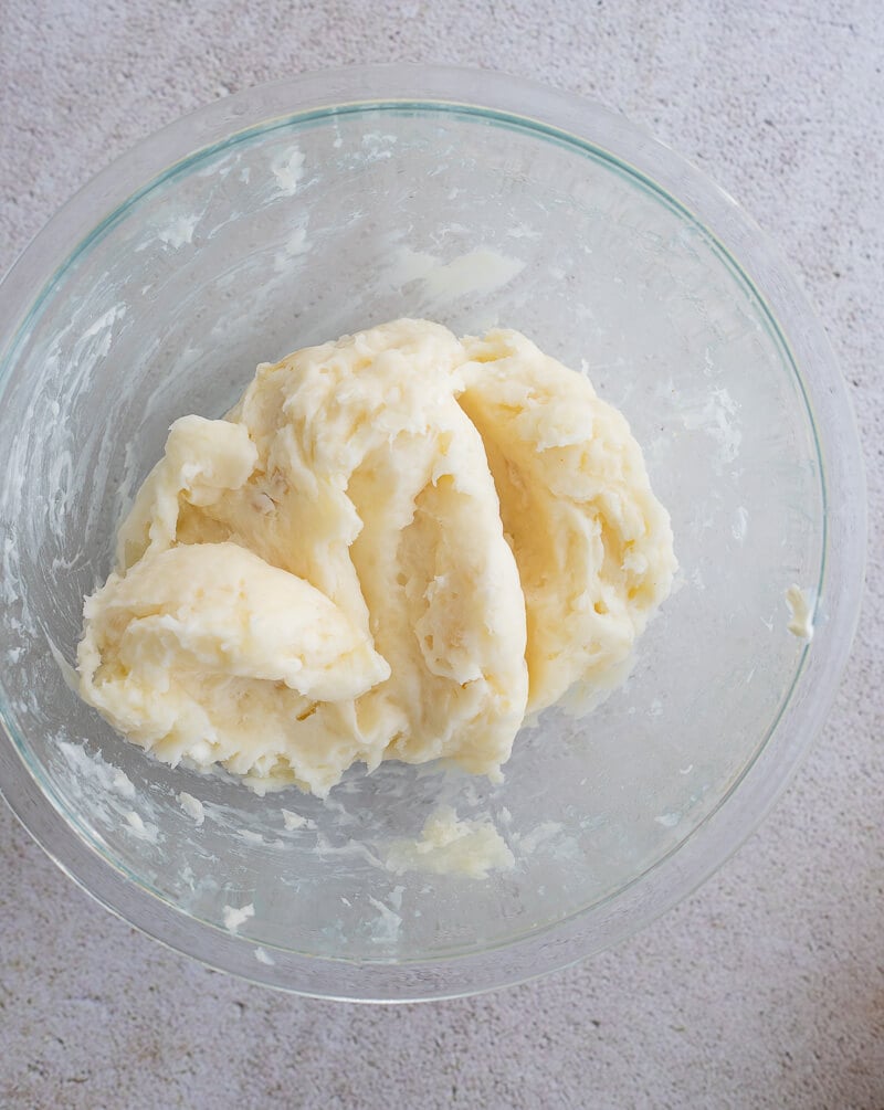 Smooth mashed cassava in a glass bowl with butter and milk, forming the creamy topping.