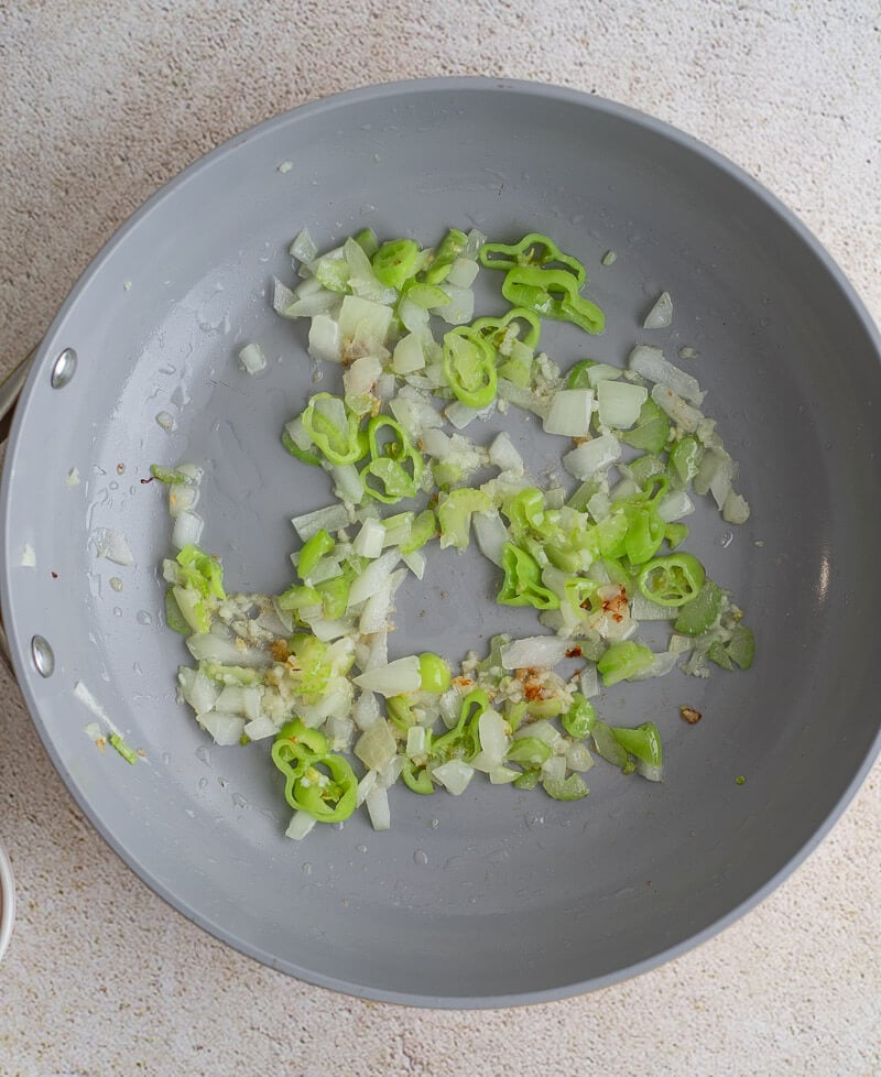 Chopped onion, celery, garlic, and hot pepper being sautéed in a grey skillet to start the beef filling.