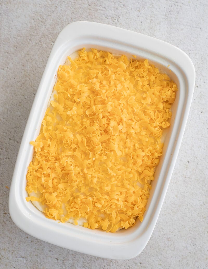 Baking dish filled with cassava shepherd’s pie topped with a generous layer of grated cheese before going into the oven.