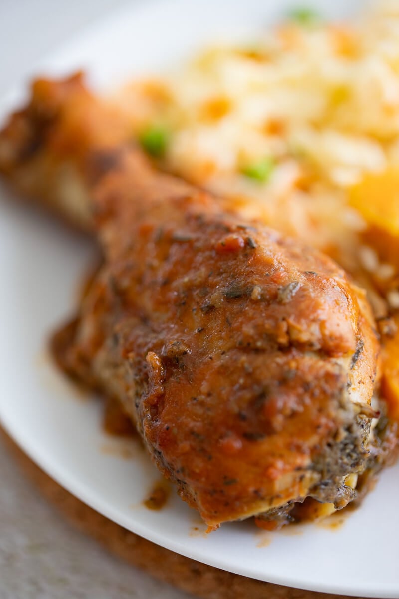 Close-up of a glazed Trinidad baked chicken drumstick served with rice and peas.