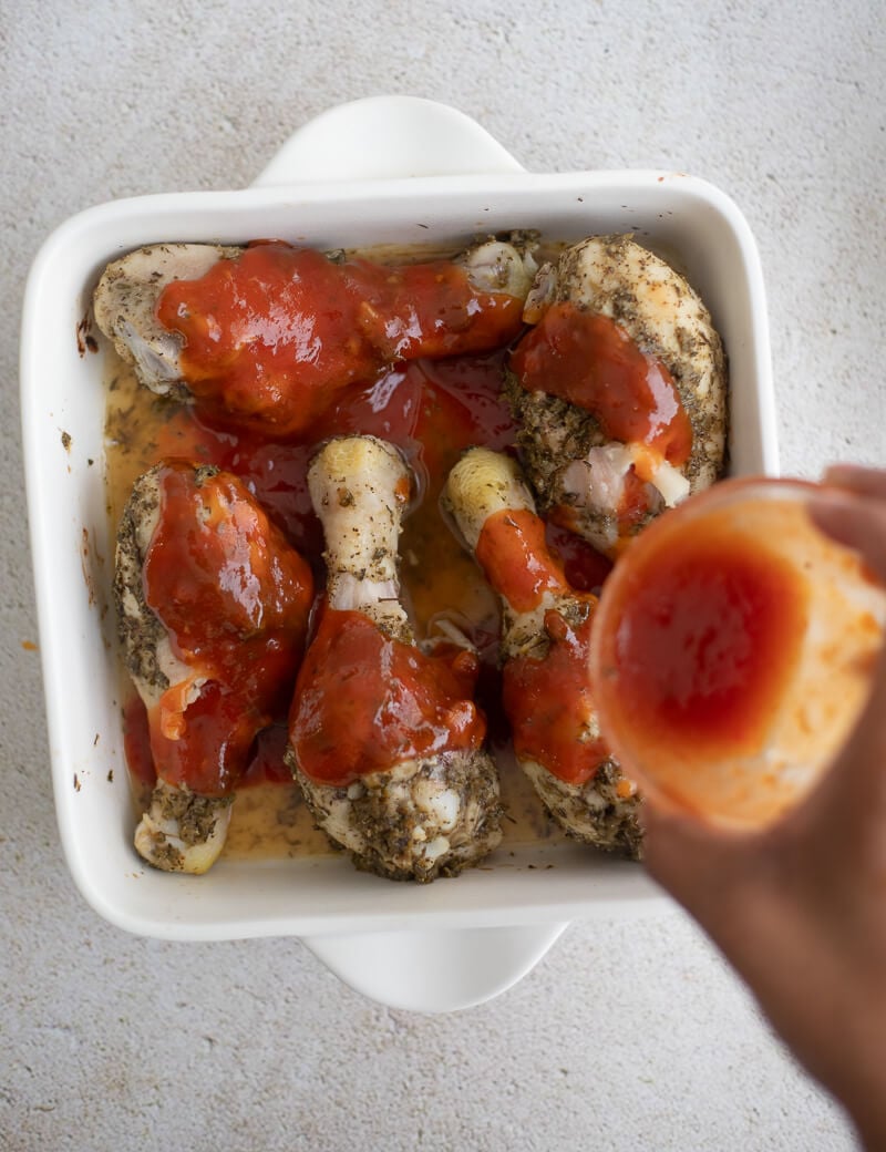 BBQ sauce being poured over chicken pieces in a white dish.