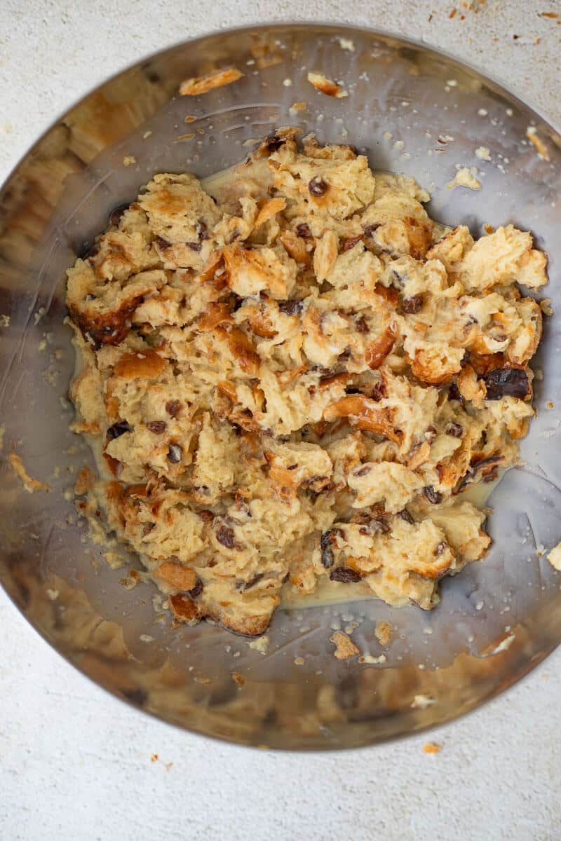 Bread cubes soaking in ponche de crème custard mixture in a large metal bowl.