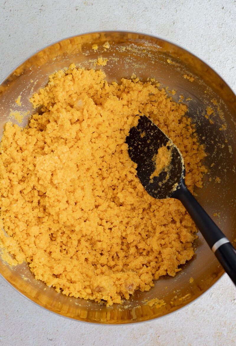 Close-up of the crumbly cornmeal mixture for Trinidad cornmeal pone showing even blending of pumpkin and sugar.