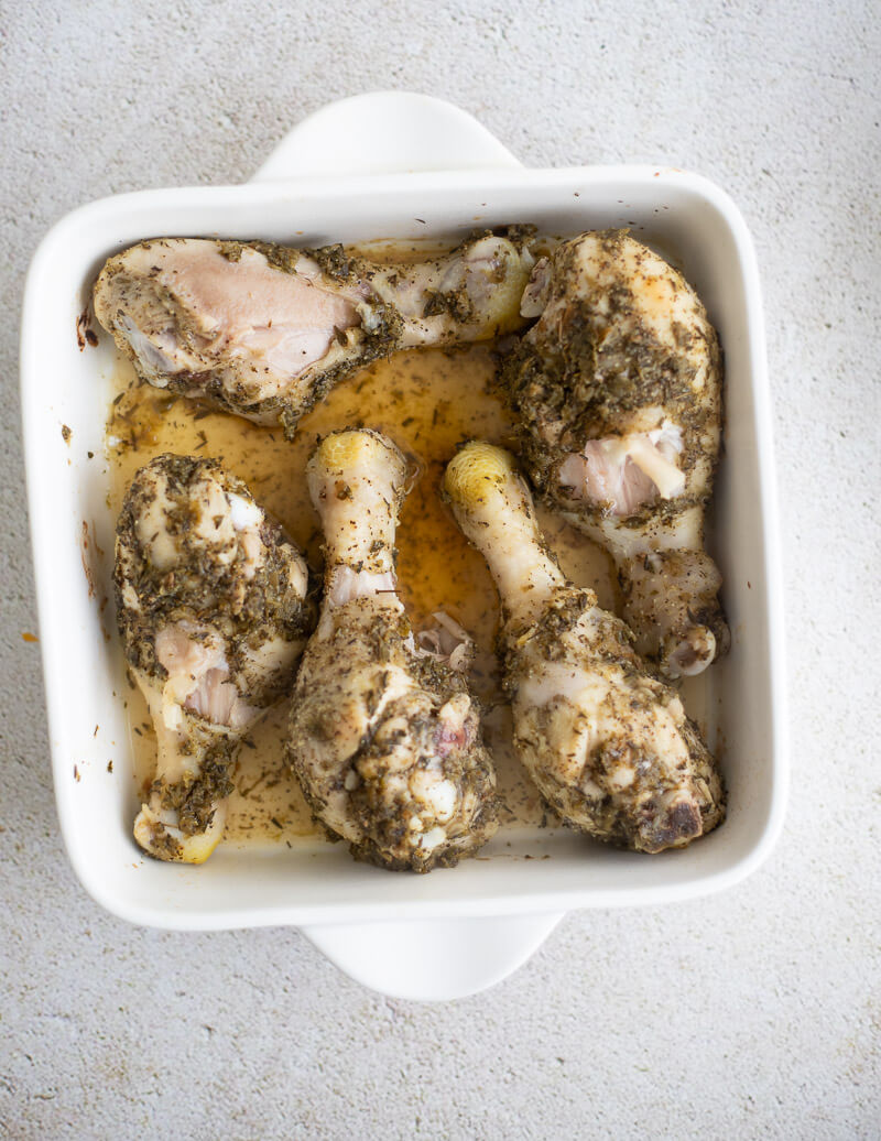 Partially baked drumstick pieces in a white dish with juices at the bottom, before adding BBQ glaze.