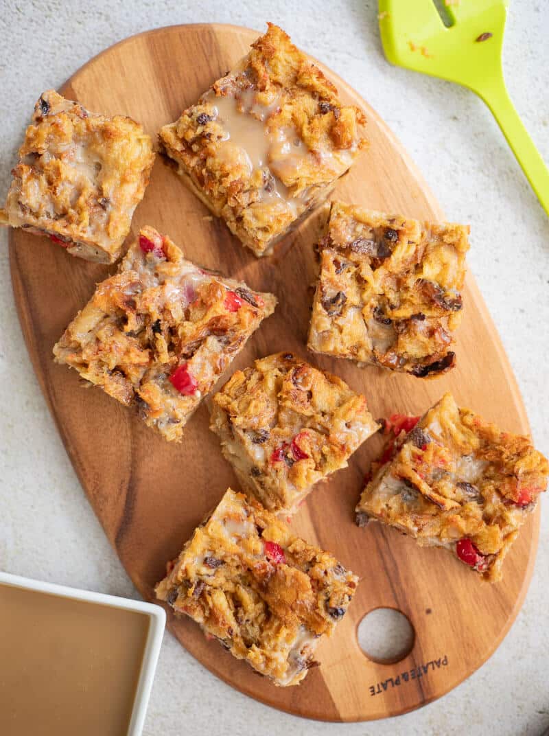 Overhead view of ponche de crème bread pudding cut into squares on a wooden serving board with glaze on the side.