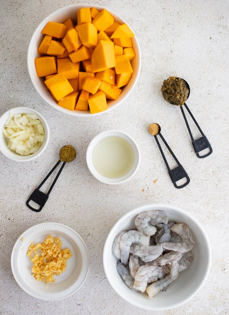 Ingredients for Caribbean pumpkin shrimp: cubed pumpkin, raw shrimp, onion, garlic, green seasoning, and oil on a light surface.