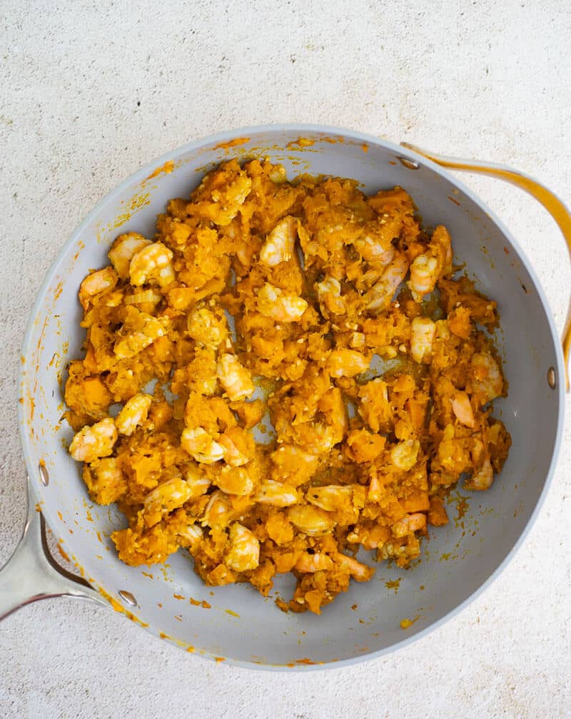 Seasoned shrimp cooking with mashed pumpkin in a skillet.