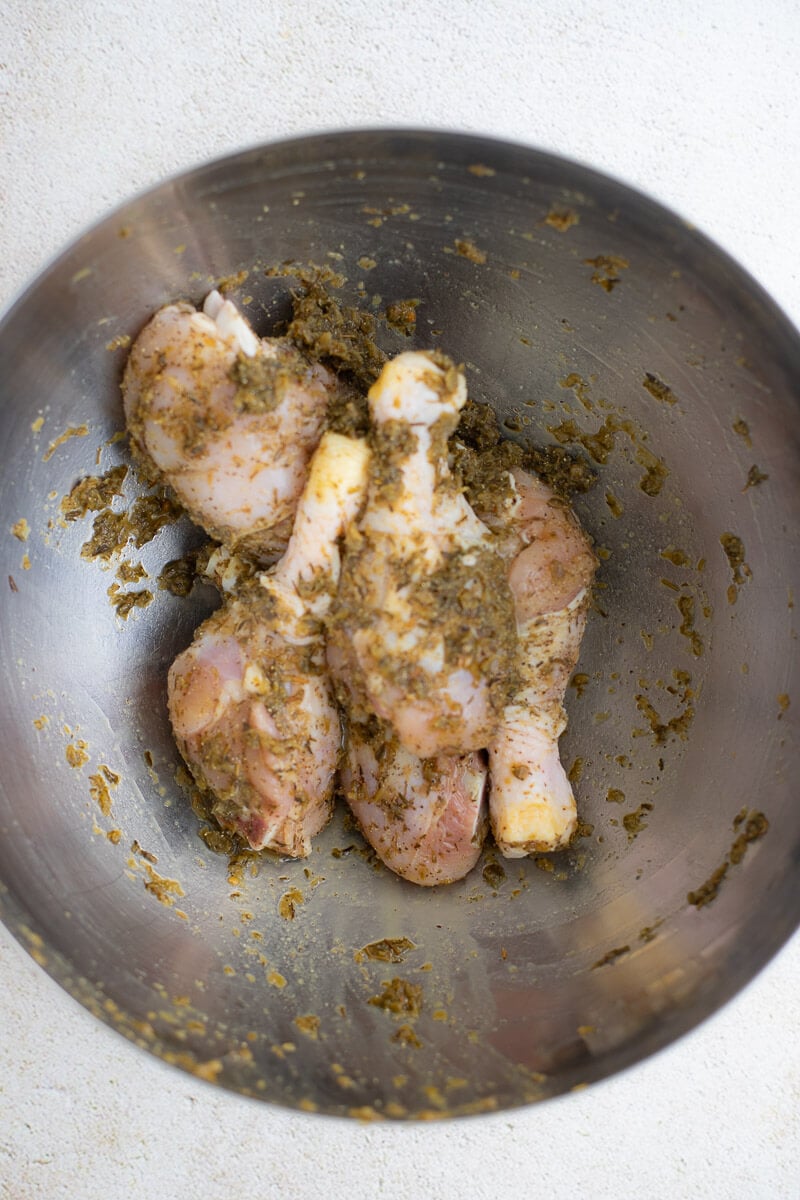 Chicken pieces marinated in Trinidad green seasoning inside a stainless steel bowl.