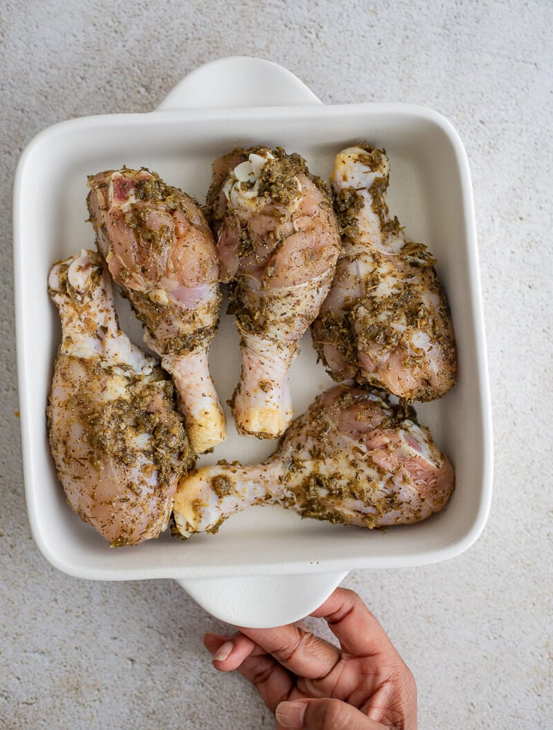 Seasoned chicken drumsticks arranged in a white baking dish, ready to be baked.